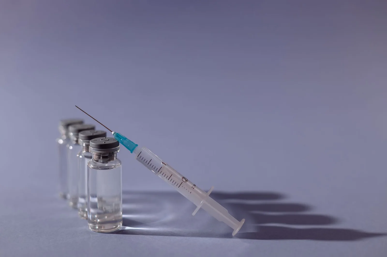 Syringe leaning on a row of glass vaccine vials