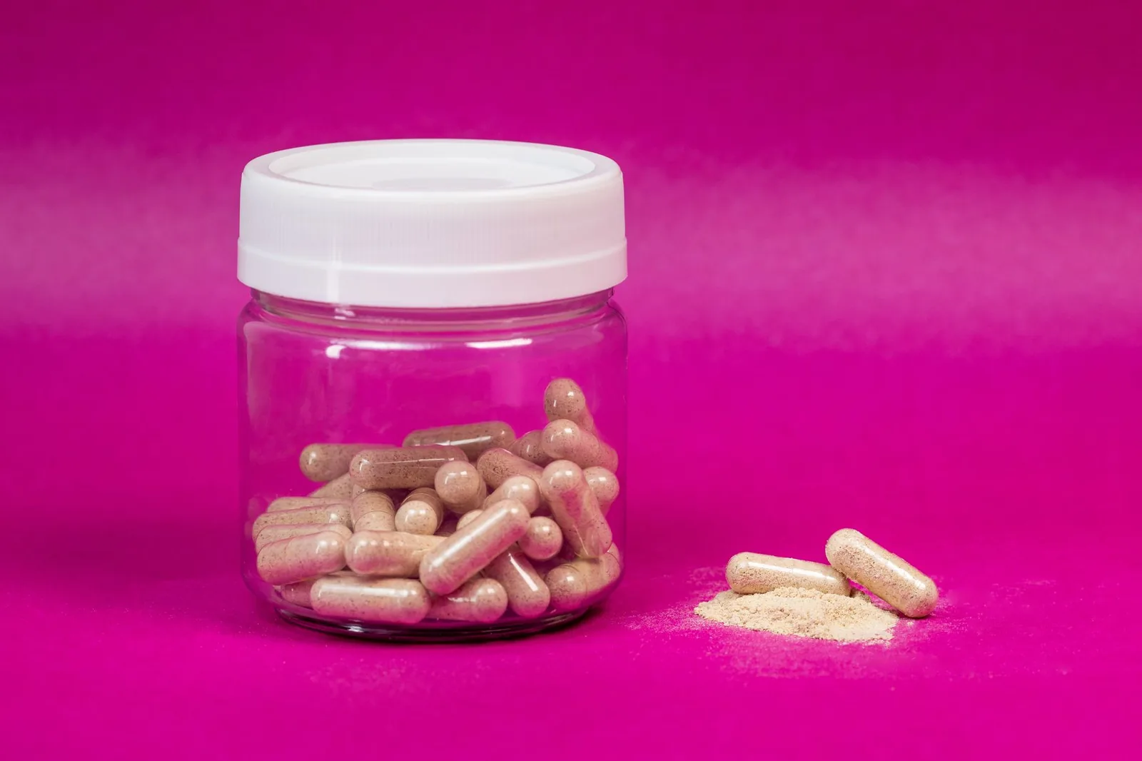 Clear jar of capsules on a pink surface