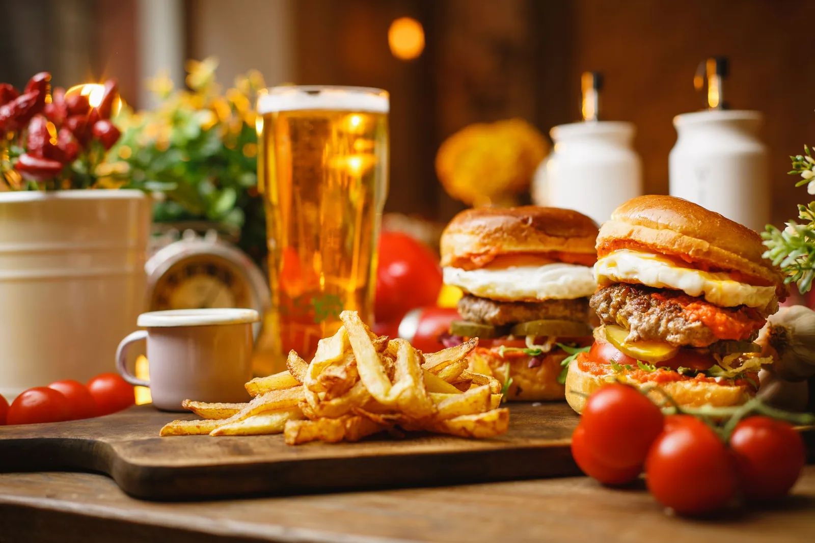 Two burgers and a pile of hand-cut fries on a wooden board beside a glass of beer.