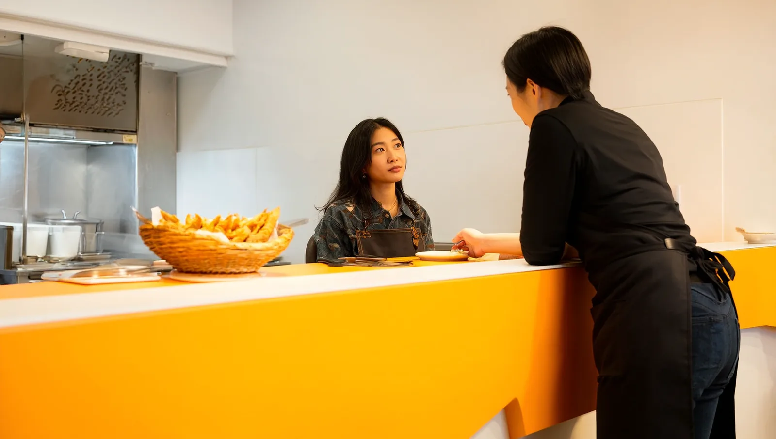 A restaurant customer leaning in to ask a staff member a question at a fast-casual counter.