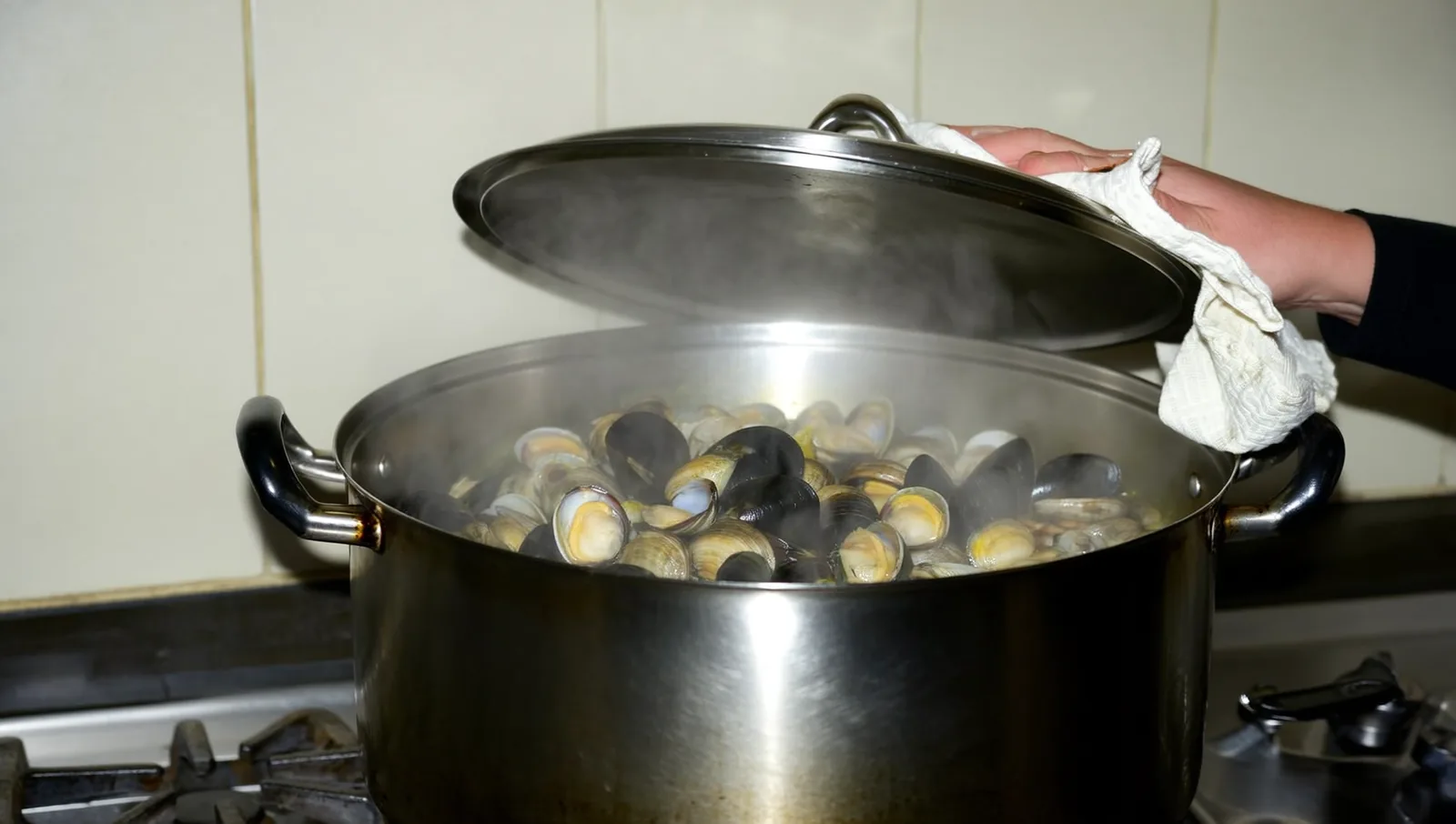 Clams steaming in an open pot on a gas stove