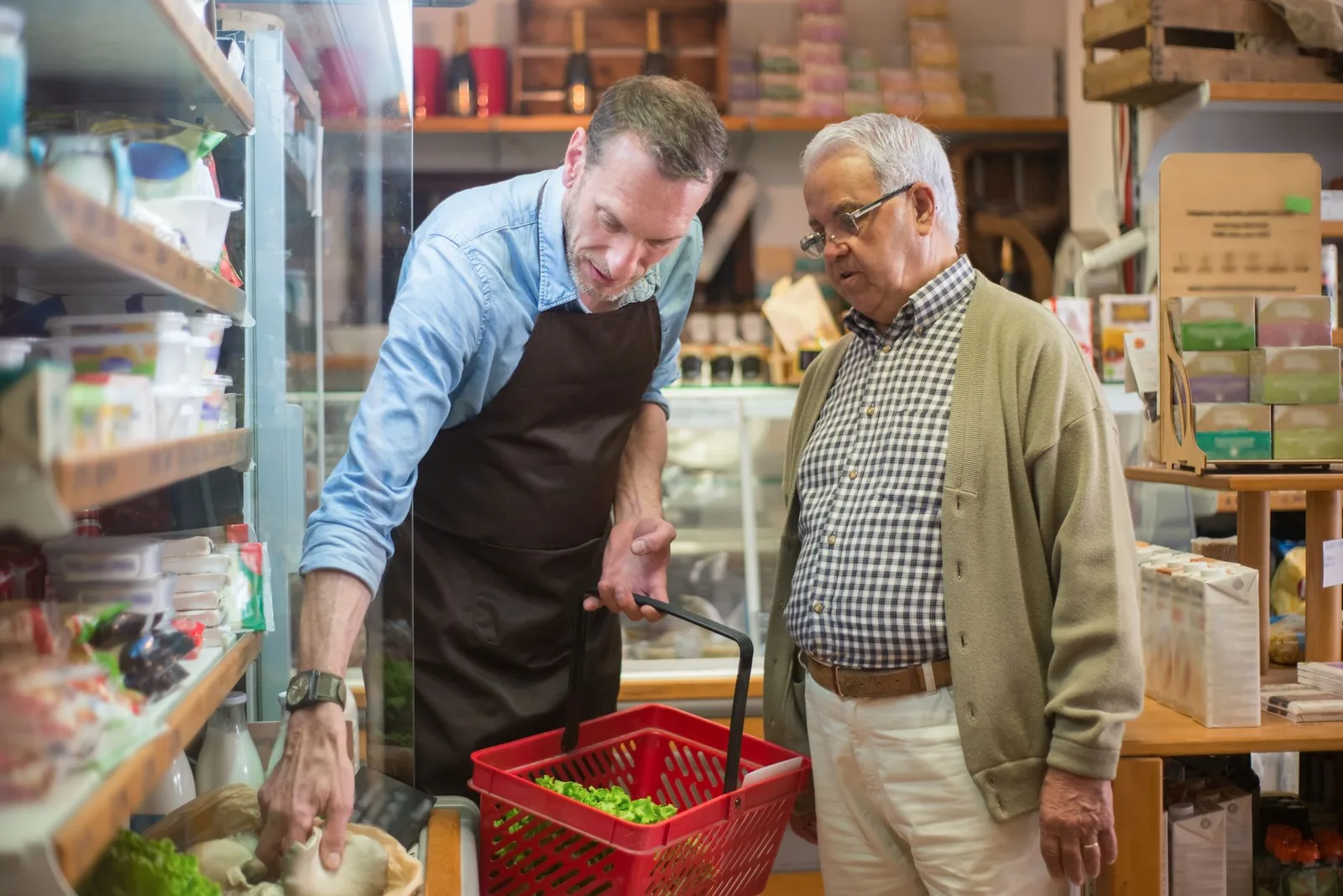 A grocery store worker helps an older shopper compare packaged products in a local store.