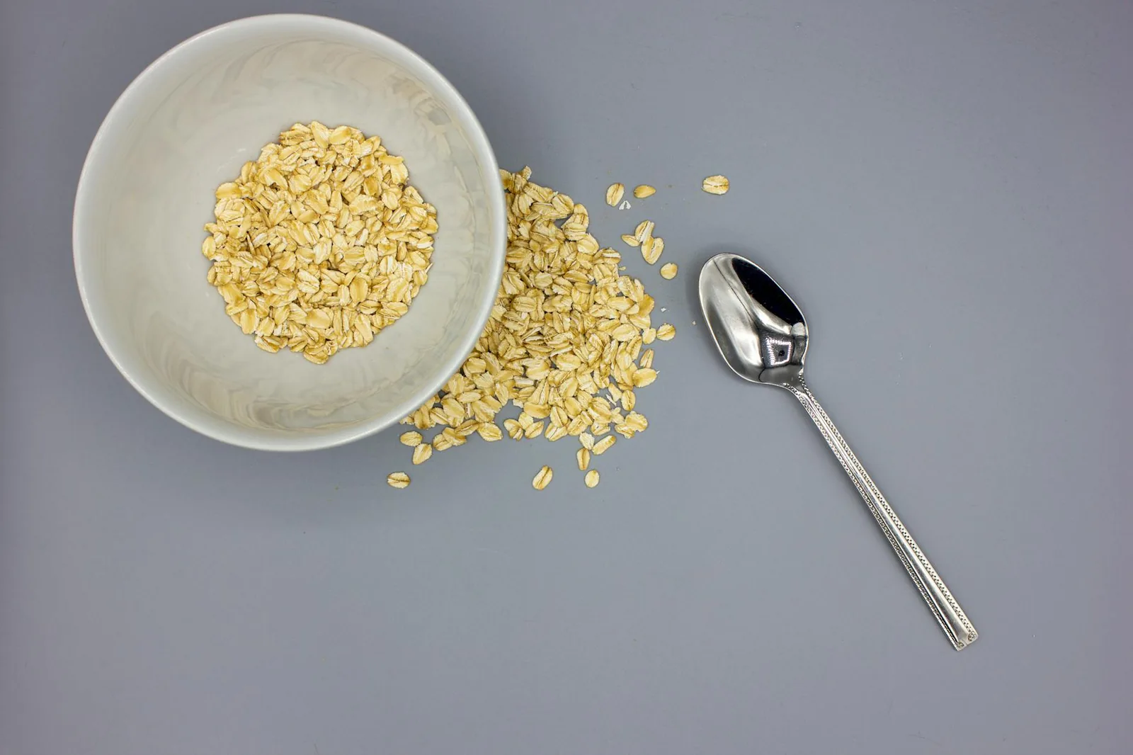 A bowl of rolled oats with a stainless spoon, viewed from above on a gray background.
