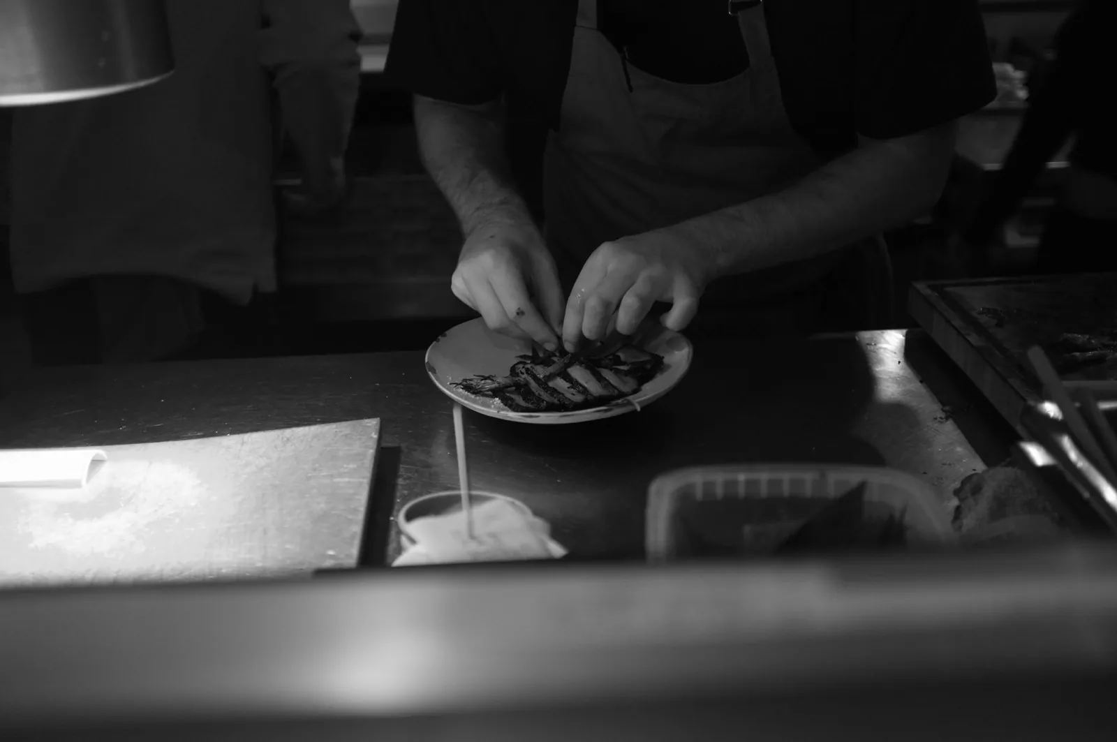 A chef plating a dish on a restaurant kitchen pass
