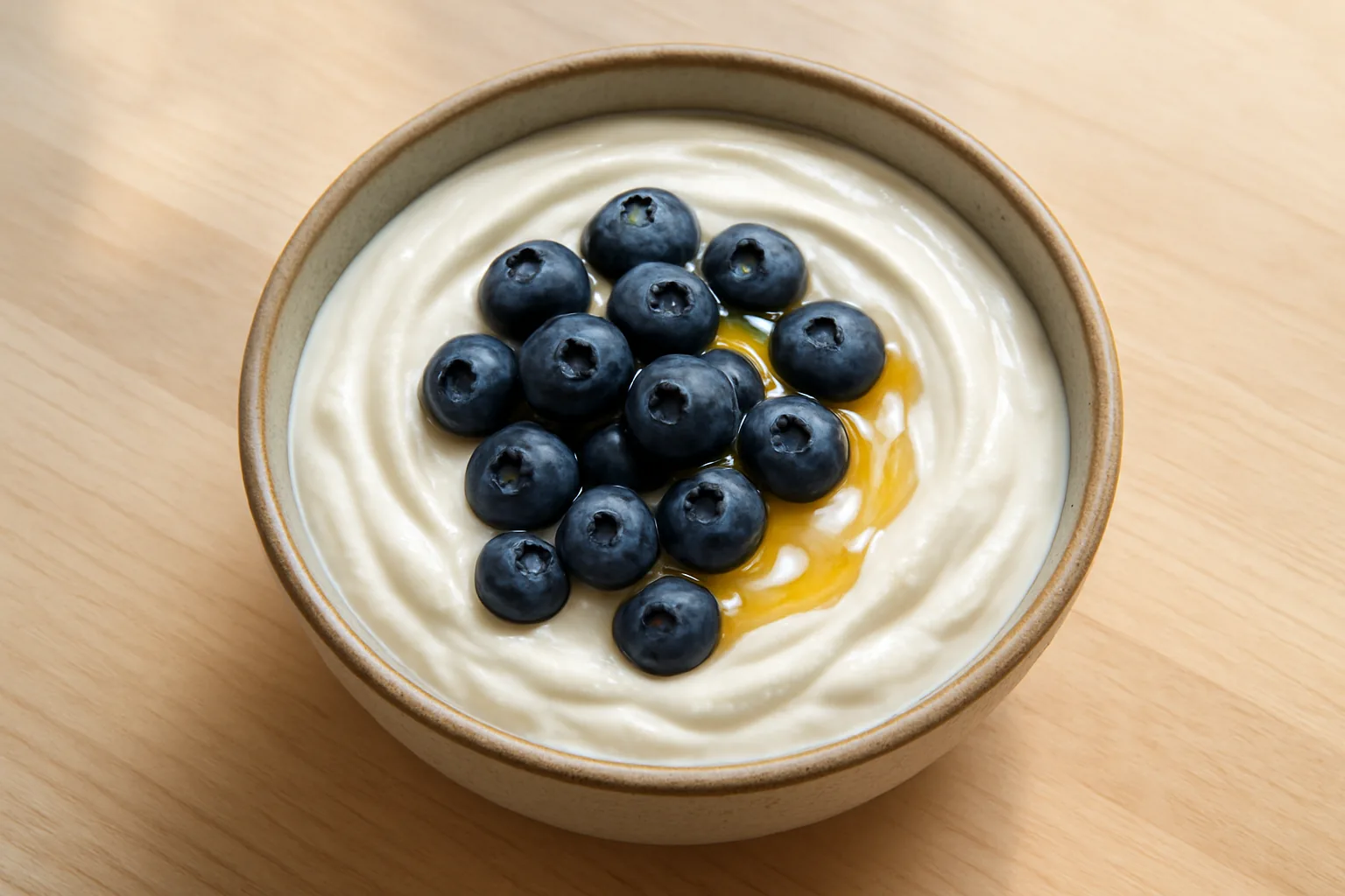 A ceramic bowl of thick plain Greek yogurt topped with fresh blueberries and a drizzle of honey.