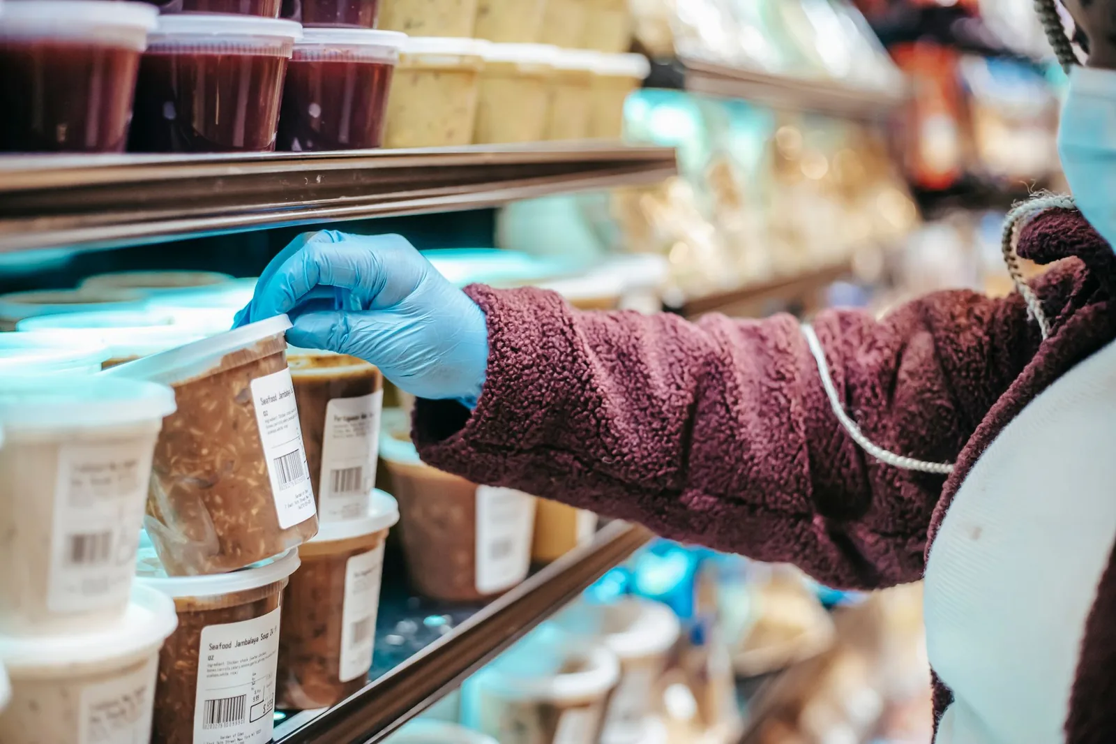 A shopper reaching into a chilled grocery case to check the label on a packaged food container.