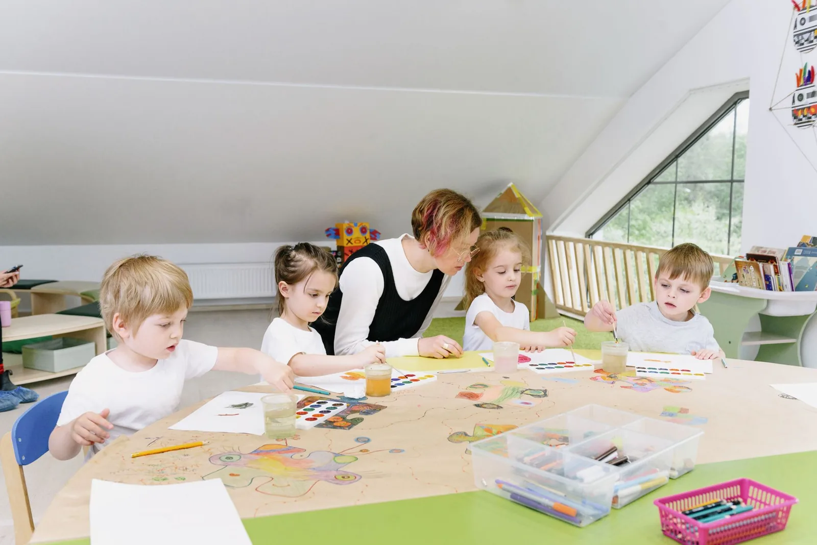 Young children engaging in art activities with a teacher in a bright kindergarten classroom.