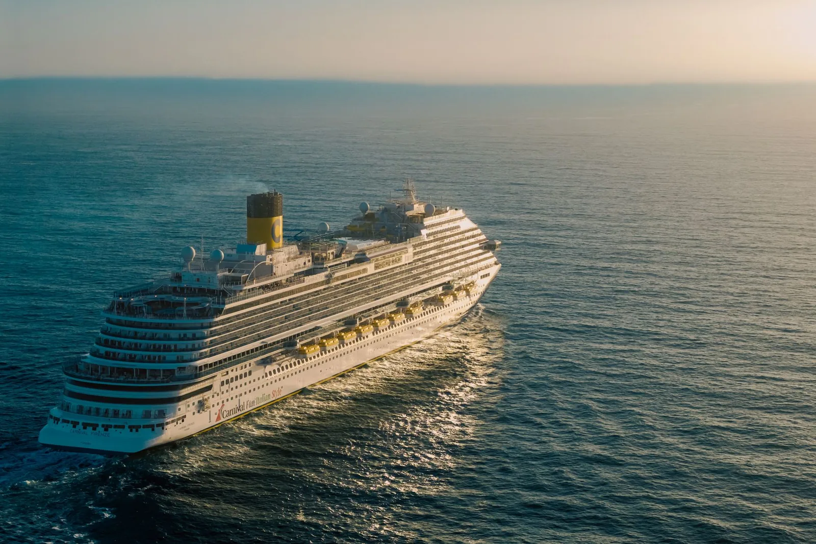 A cruise ship sailing across the open ocean at sunset.