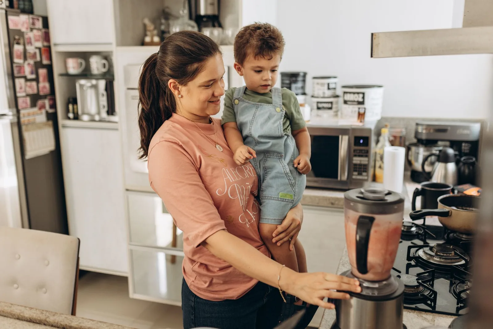 A parent holding a toddler while using a kitchen blender